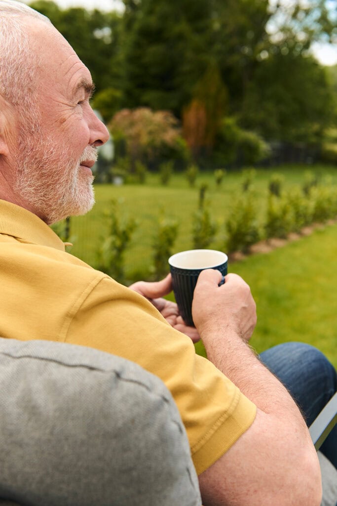 Kunde genießt die Betreuungszeit im Park mit dem Pflegehelfer beim Kaffetrinken