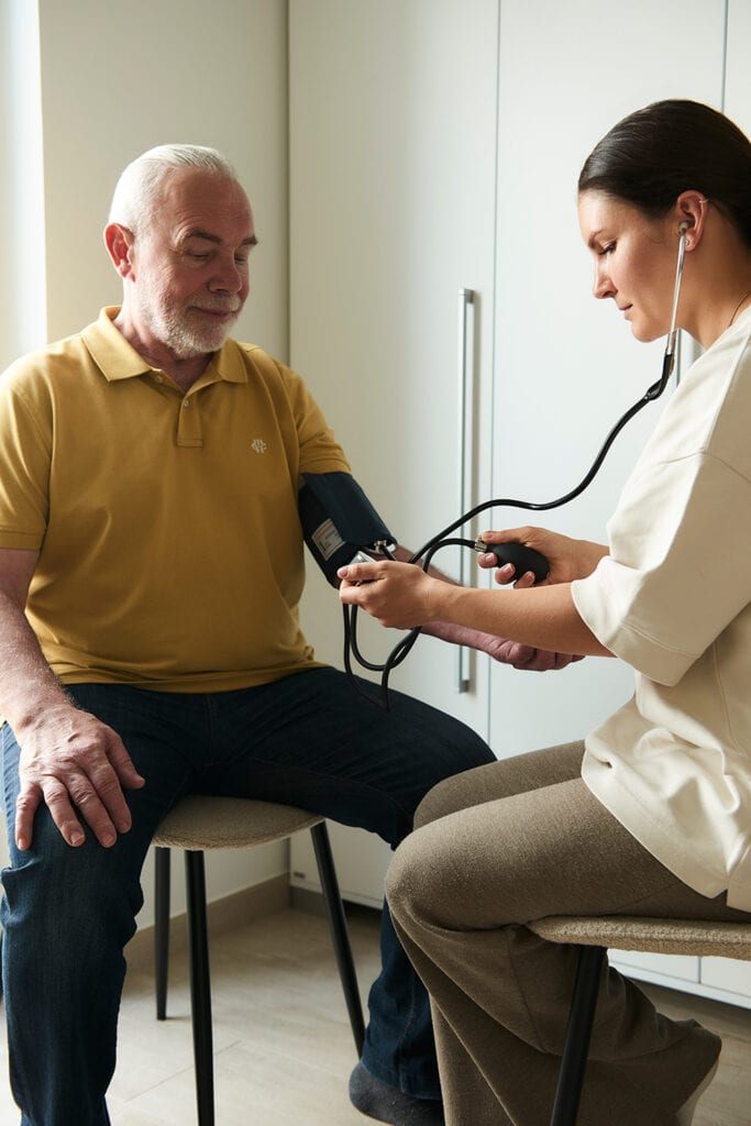 Pflegefachkraft unterstützt den Kunden bei der Blutdruckmessung